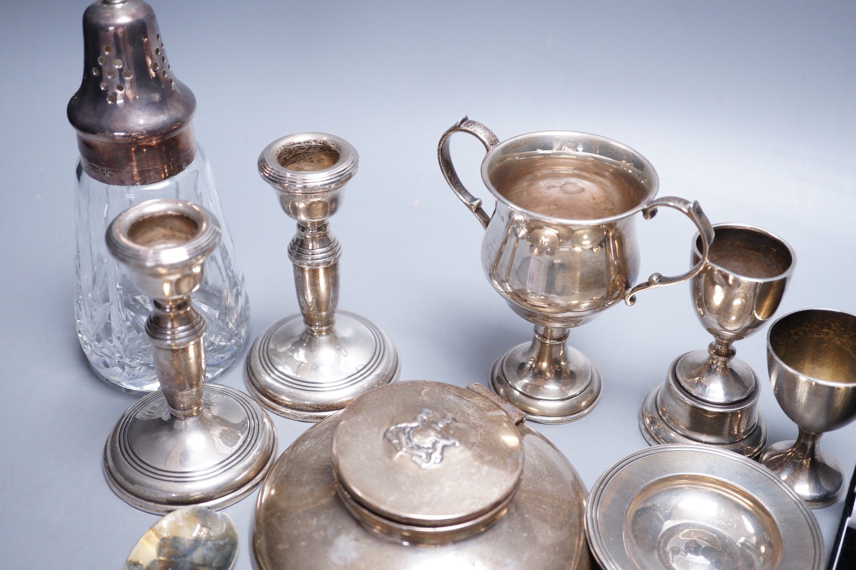 A small collection of assorted small silver, including a capstan inkwell, pair of dwarf candlesticks, two small trophy cups, egg cup, flatware, napkin ring, glass caster, a modern parcel gilt silver stag brooch and three